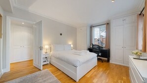 A bedroom with a bed, a desk, and a chair. There is a window with blinds and a door.