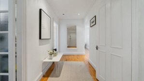 A hallway with white walls, a wooden floor, a white door, and a small table with a vase of flowers.