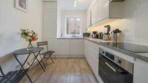A compact kitchen with white cabinets, a built-in oven, and a window overlooking a brick building.