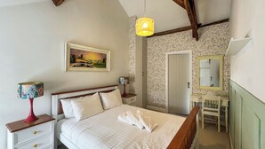 Un dormitorio con cama, mesitas de noche, lámpara, cuadro, espejo y puerta.