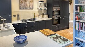 Una cocina moderna con armarios oscuros, una estufa a gas, horno integrado y una estantería con libros.