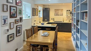 Un comedor con una mesa y sillas de madera, una cocina al fondo y una estantería llena de libros.