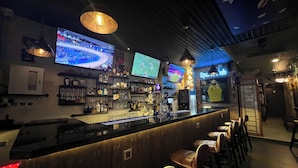 Uma área de bar com várias telas exibindo eventos esportivos, uma variedade de garrafas de bebidas alcoólicas e um telefônico.