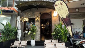 Restaurante com mesas ao ar livre, fachada de pedra e placa com a inscrição 'KNK Homestay & Sports Pub'.