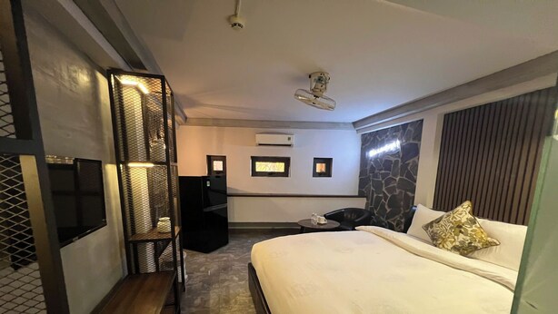 Quarto de hotel moderno com uma cama grande, área de estar, uma mesinha e televisão integrada.