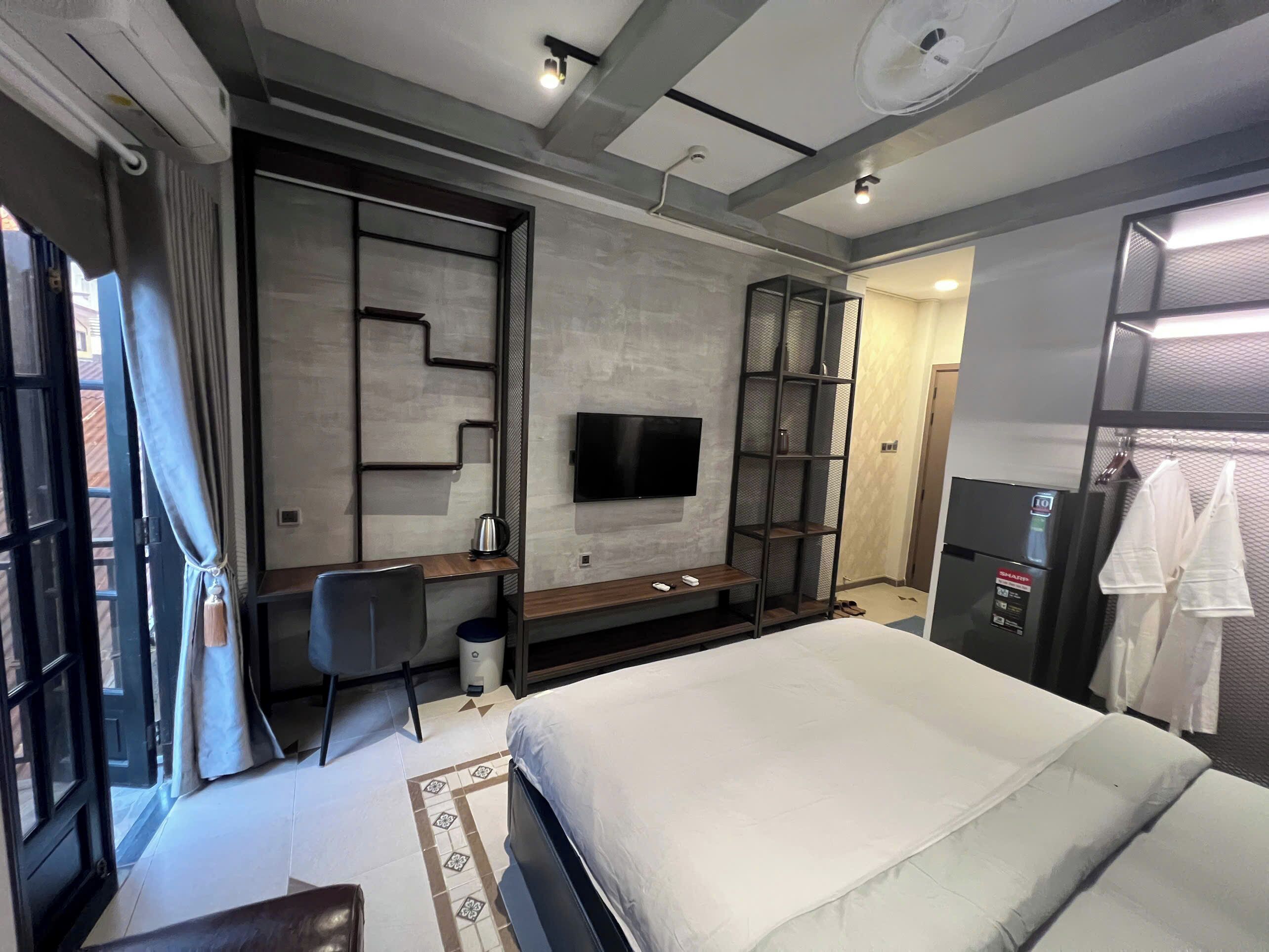 A modern hotel room with a bed, a desk, a TV, a wardrobe, and a shower area.