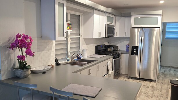 A modern kitchen with white cabinets, stainless steel appliances, and a central island with bar stools. - 4-bedroom oasis in amazing Hatillo (Barrio pueblo)