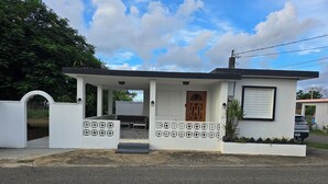 A small, single-story building with a porch, a wooden door, and a white exterior. - 4-bedroom oasis in amazing Hatillo (Barrio pueblo)