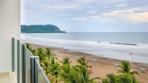 A beach view from a balcony with palm trees, beach umbrellas, and flags. - Diamante del sol 601N (Jacó)