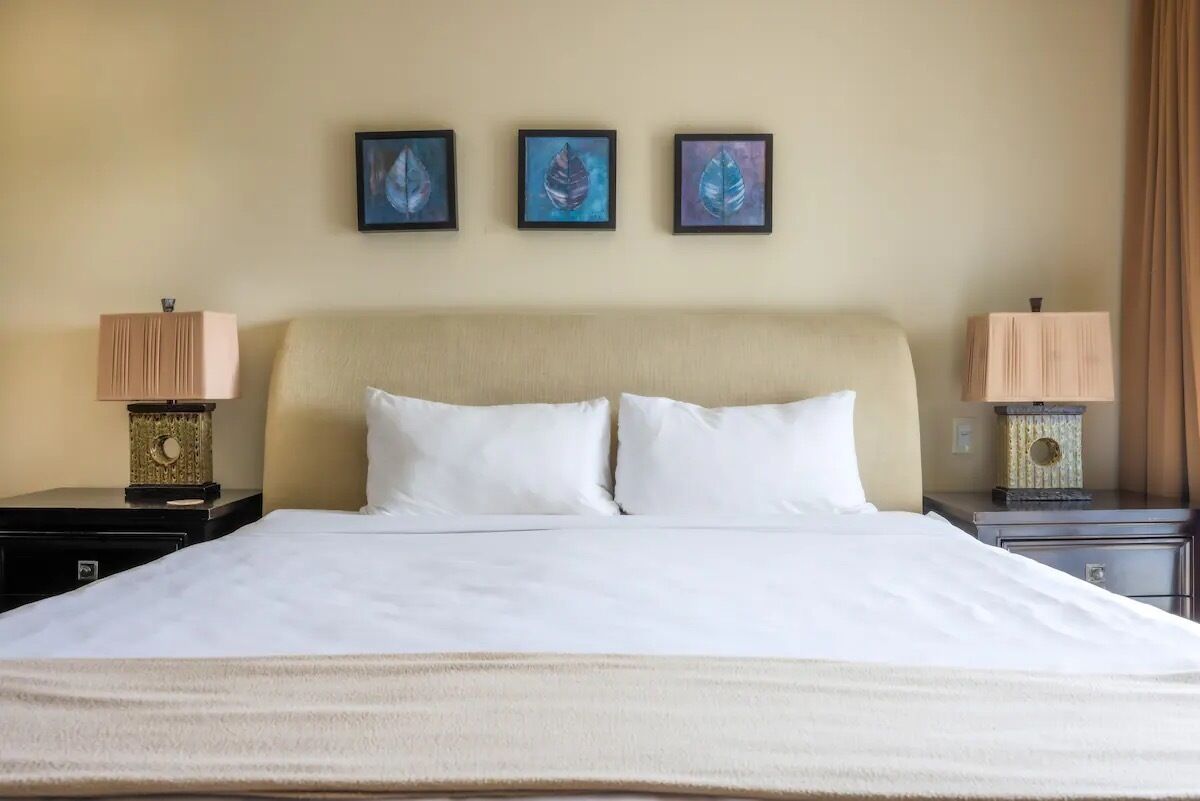 A hotel room with a large bed, two bedside tables with lamps, and three framed artworks on the wall.