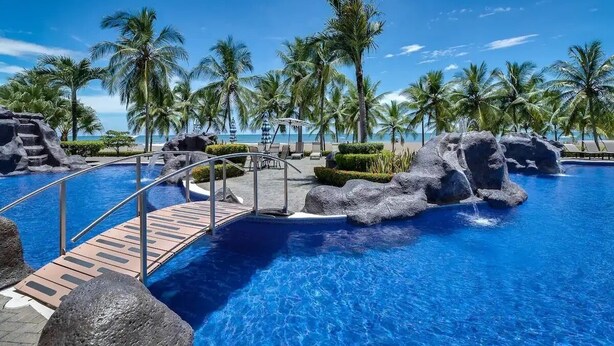 A swimming pool with rock formations and palm trees. - Diamante del sol 601N (Jacó)
