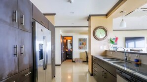 A modern kitchen with dark cabinets, a stainless steel refrigerator, a sink, and a clock on the wall. - Diamante del sol 601N (Jacó)