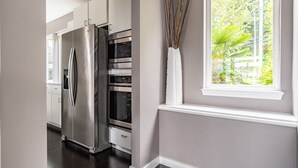 A kitchen with a stainless steel refrigerator, built-in oven, and a window with a view of greenery. - Majestic Views with a Hot Tub! (Seattle)