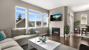 A modern living room with a large window, a fireplace, and a view of a cityscape. - Majestic Views with a Hot Tub! (Seattle)