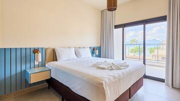 A hotel room with a large bed, a nightstand, a lamp, and a view of the ocean through a large window.