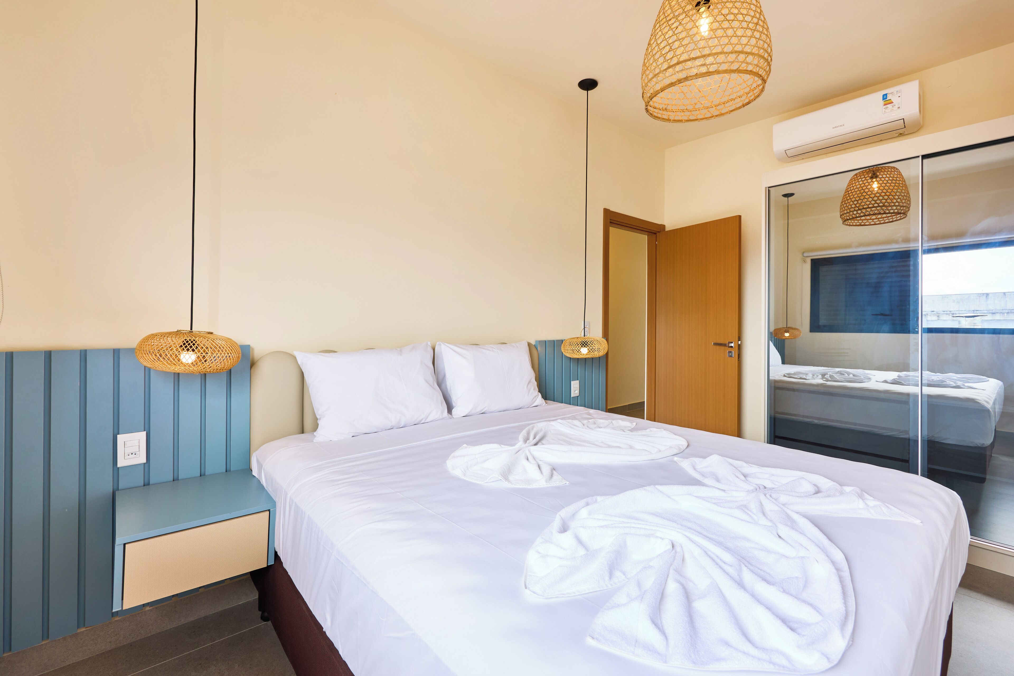 A neatly made bed with white linens, a bedside table, and a wall-mounted air conditioner.