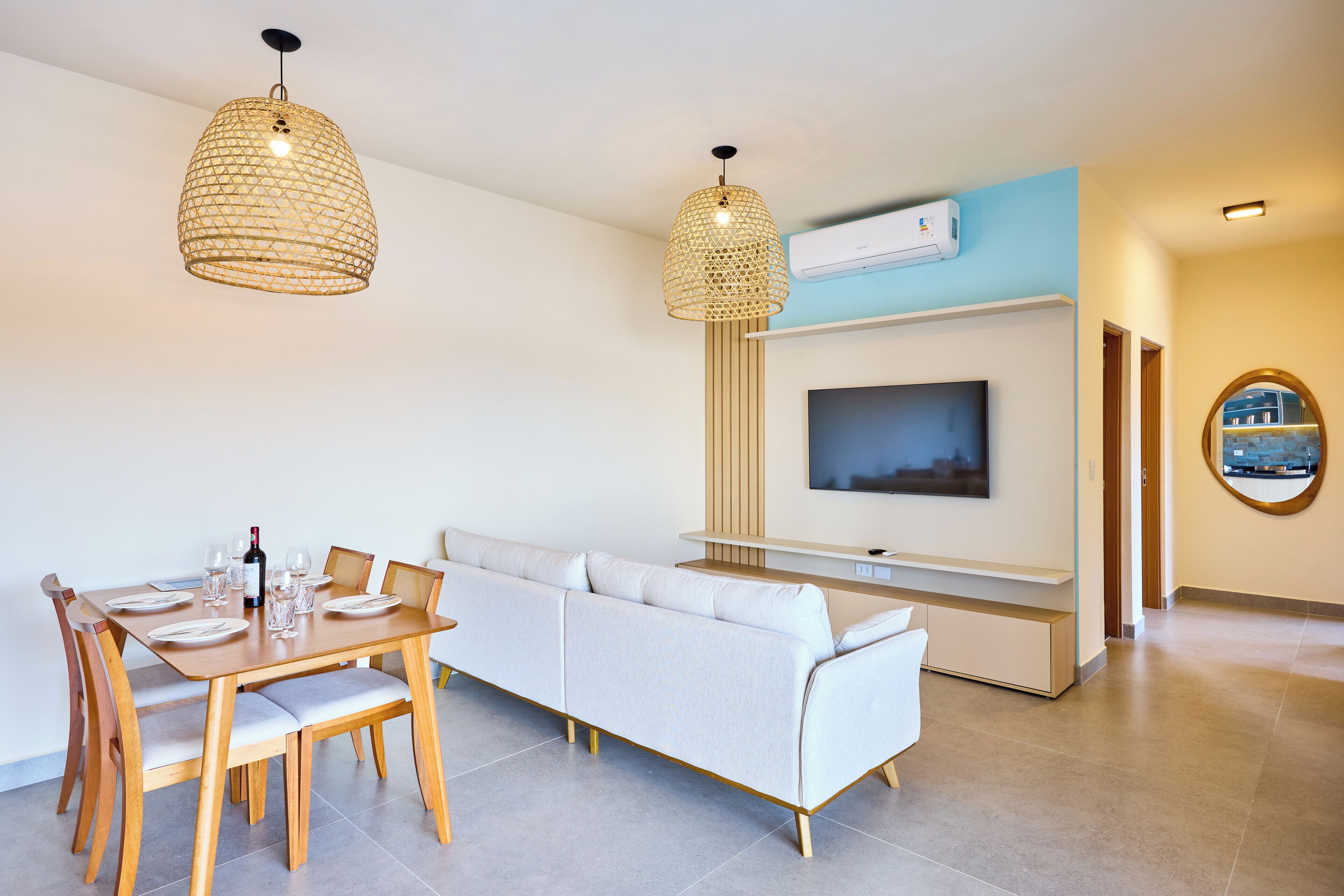 A modern living room with a dining area, a sofa, a TV mounted on the wall, and a ceiling fan.