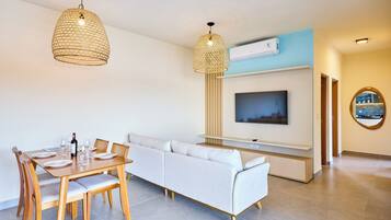 A modern living room with a dining area, a sofa, a TV mounted on the wall, and a ceiling fan.