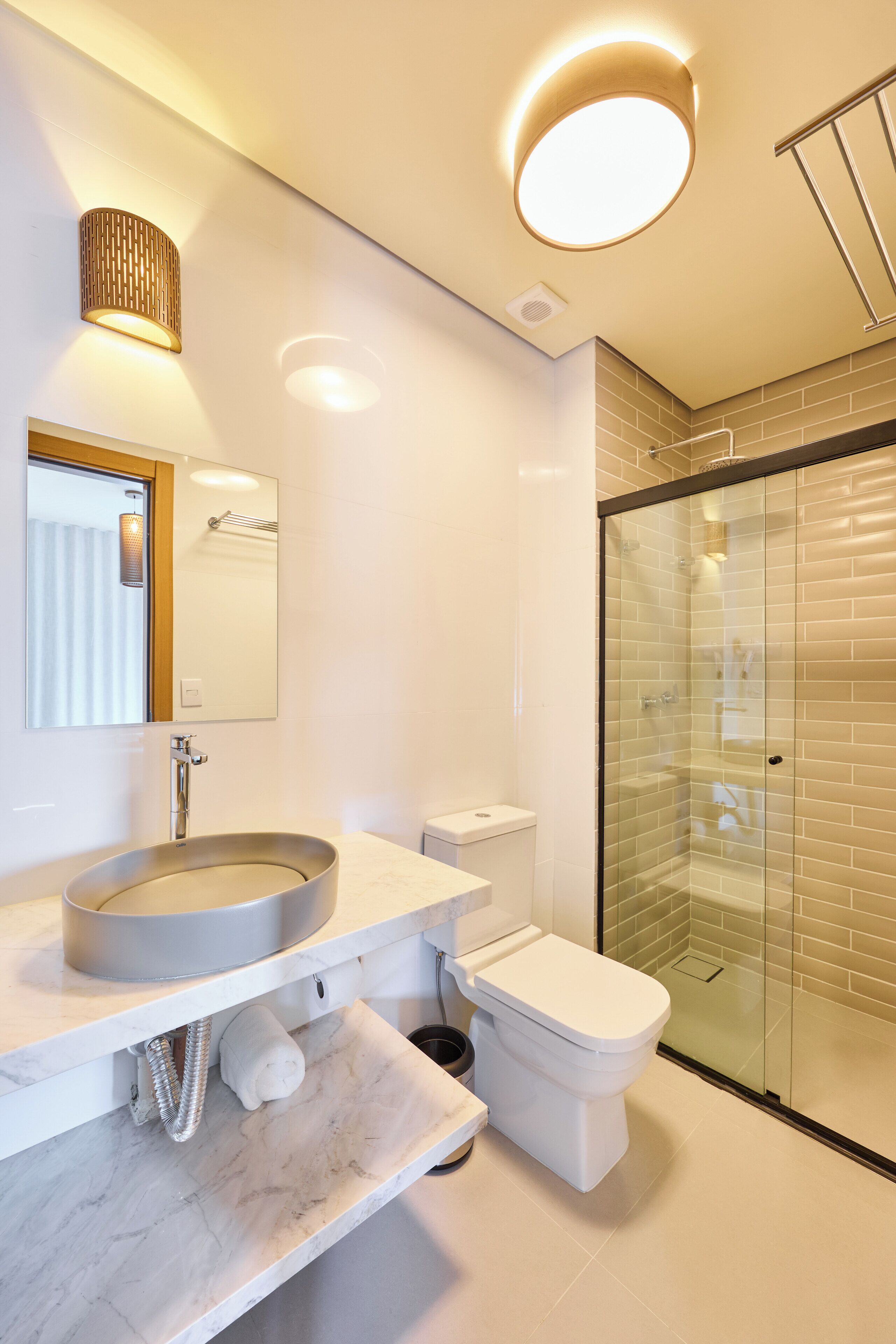A modern bathroom with a round sink, a toilet, a glass shower enclosure, and a mirror with a wooden frame.