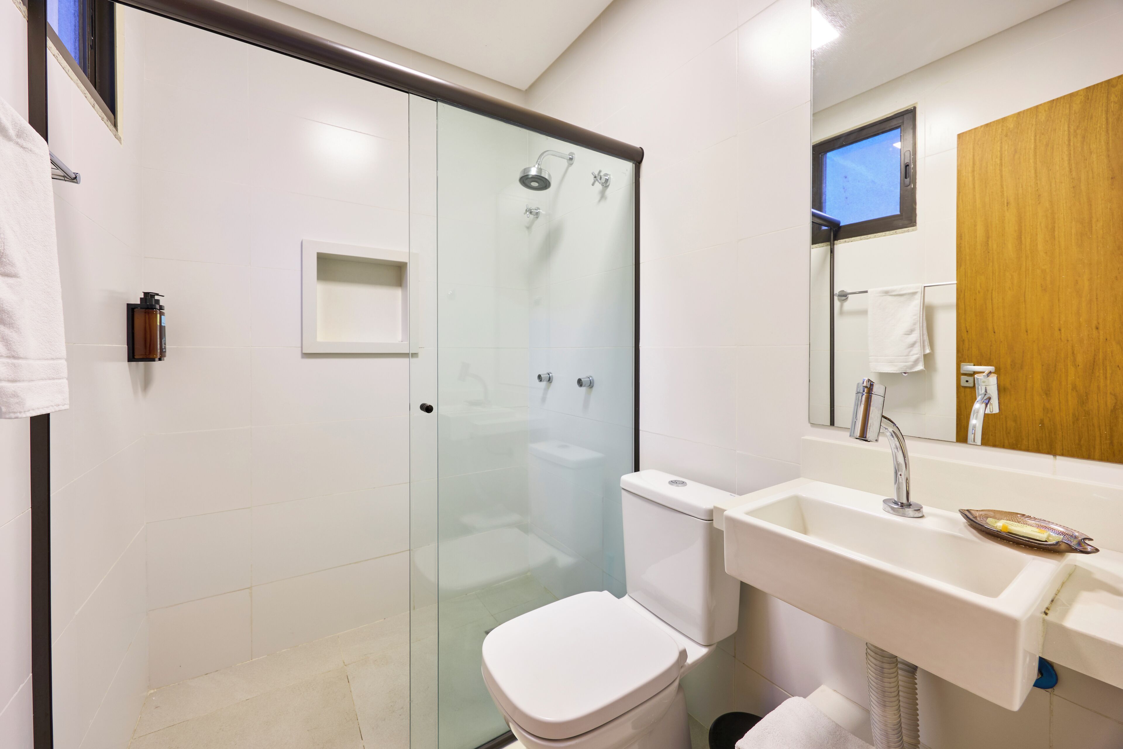 A modern bathroom with a glass-enclosed shower, a white toilet, a sink with a soap dish, and a wooden door.
