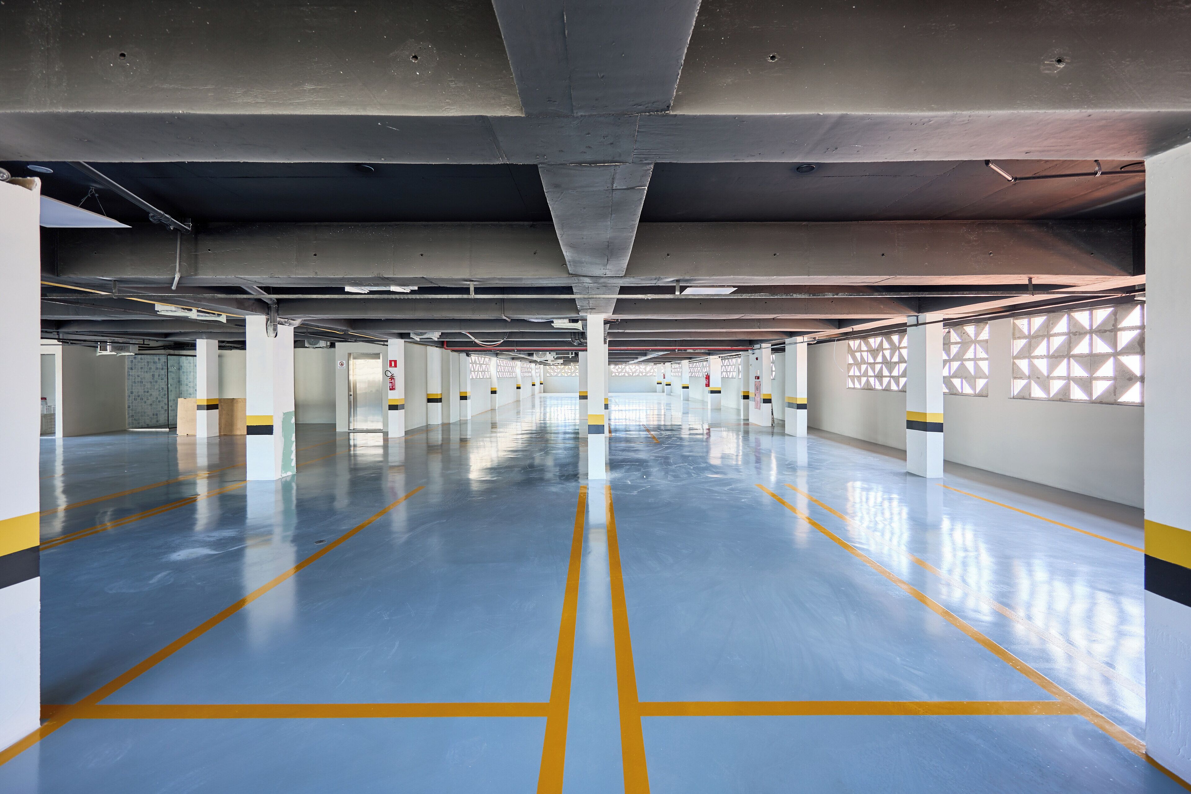 A spacious parking garage with a blue floor and yellow lines, featuring white pillars and a geometric wall pattern.