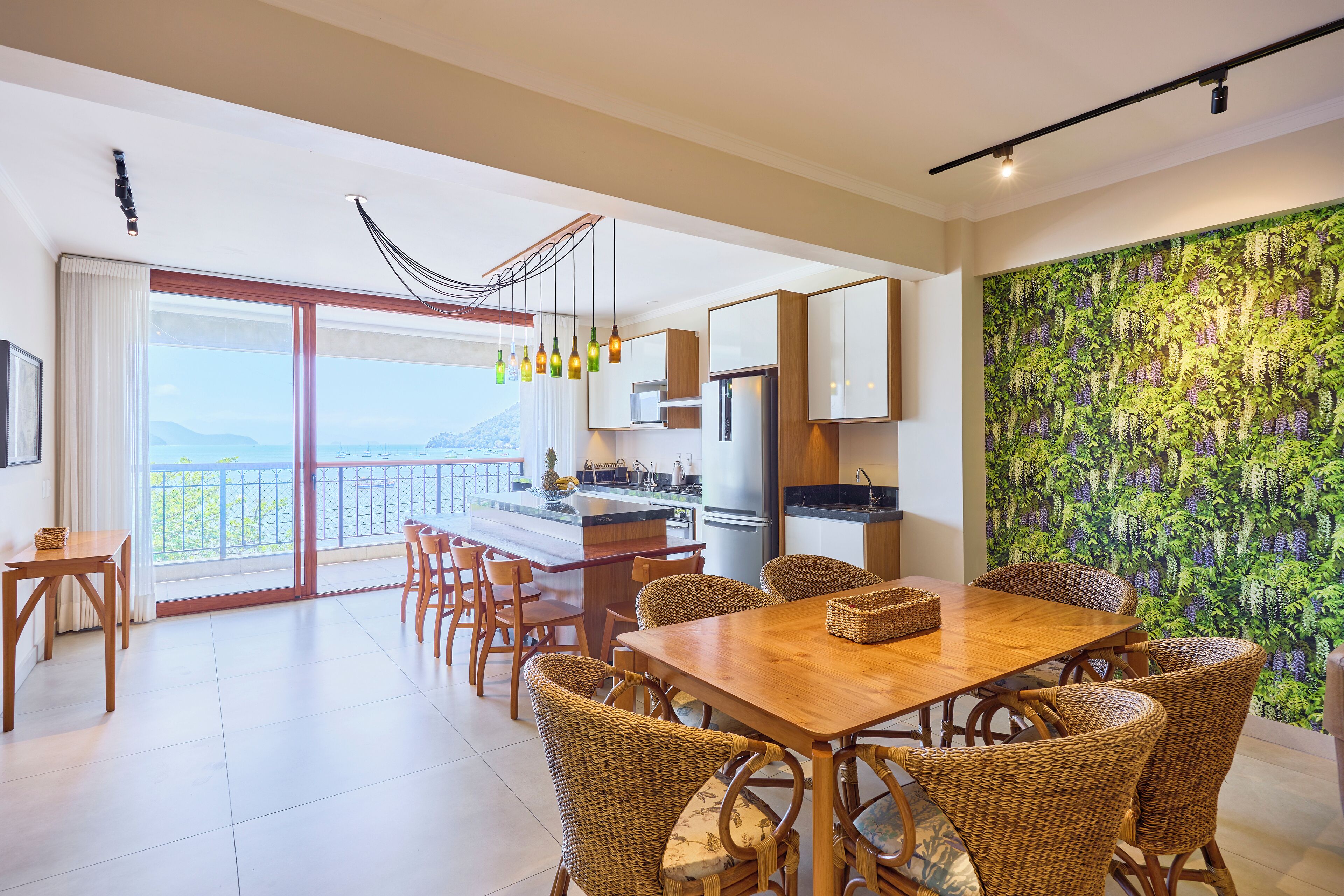 Una cocina moderna con una isla grande, comedor con sillas de mimbre y vista al exterior.