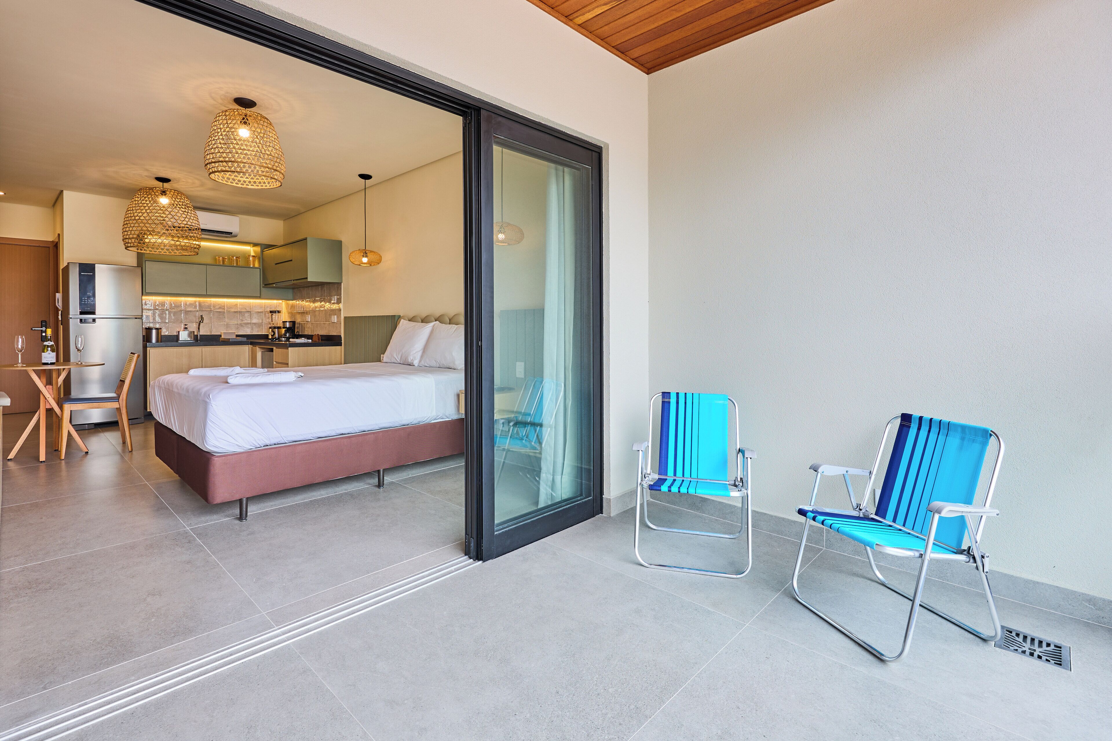 Une chambre d’hôtel moderne avec un lit, une porte vitrée donnant sur une cuisine et deux chaises à rayures bleues.