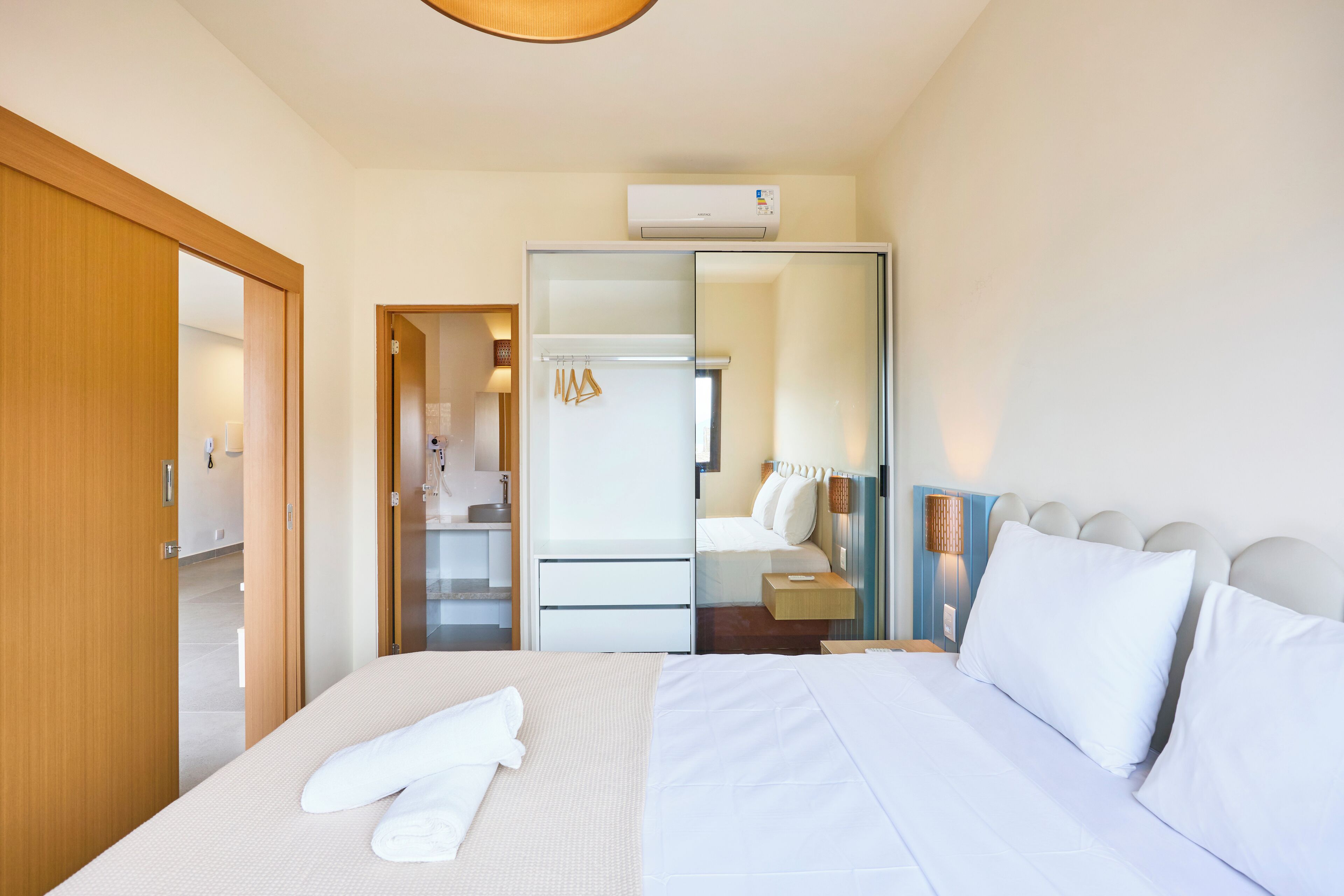 Une chambre d’hôtel comprenant un lit, une armoire, un miroir et une salle de bain visible à travers une porte en verre.