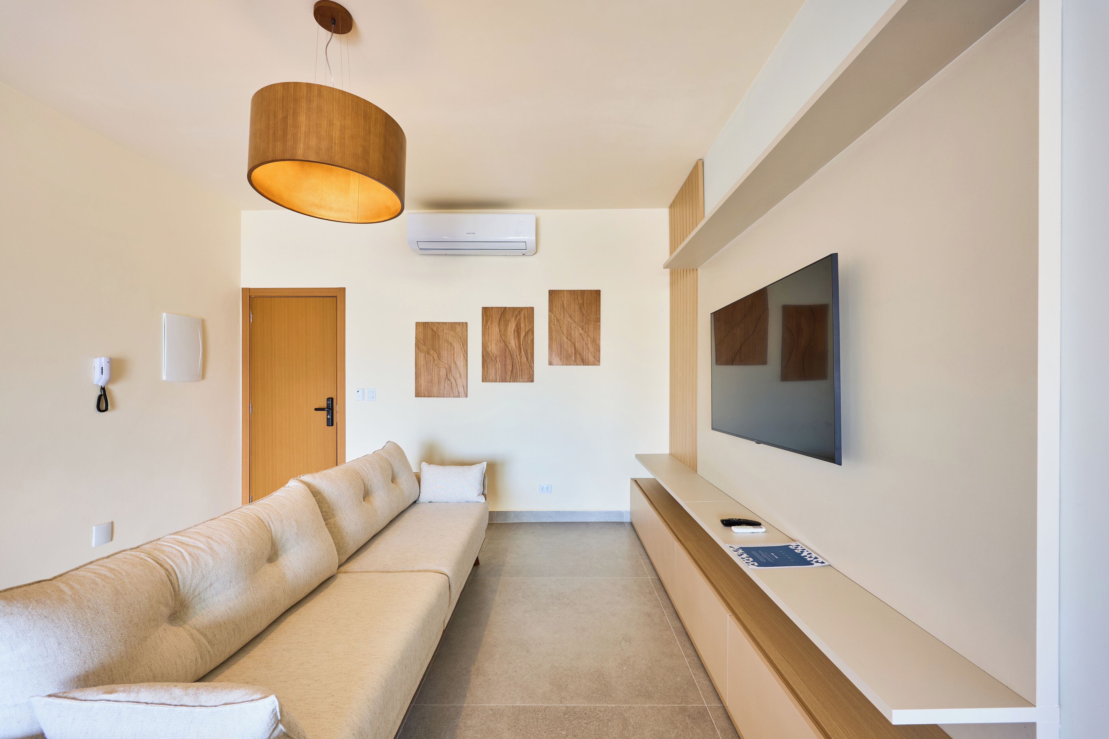 Ein modernes Wohnzimmer mit einer Couch, einem an der Wand montierten Fernseher, einer Holzzudecke und einer Tür im Hintergrund.