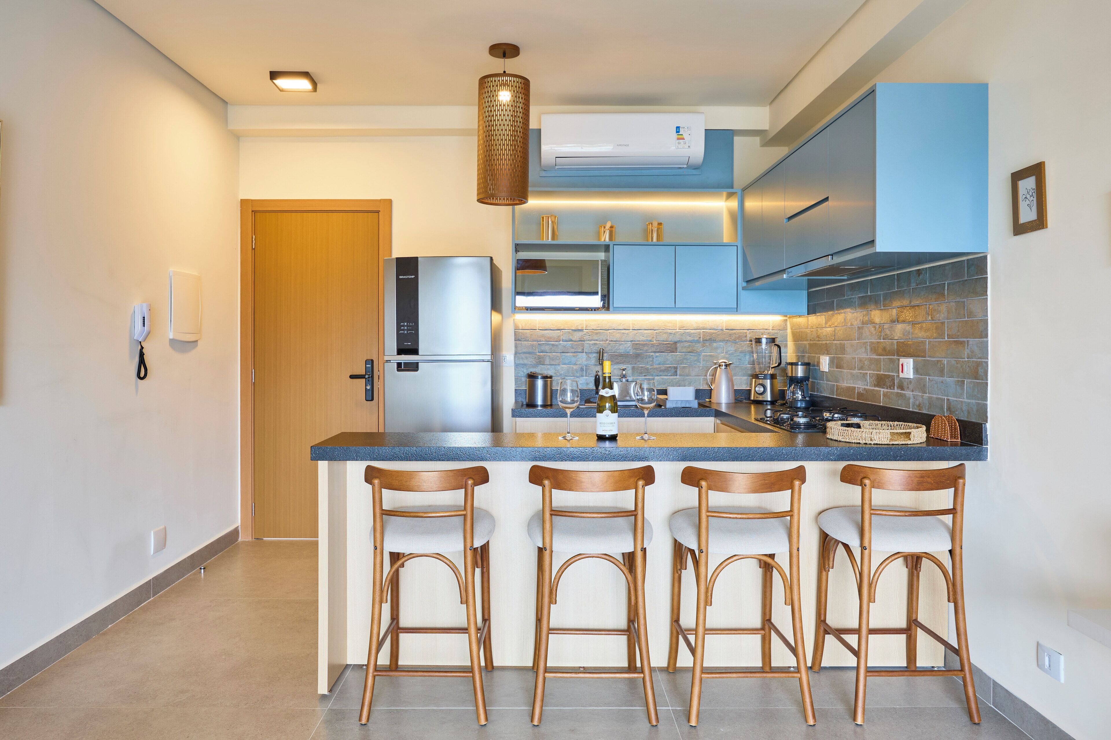 A modern kitchen with a central island, bar stools, stainless steel appliances, and a hanging light fixture.