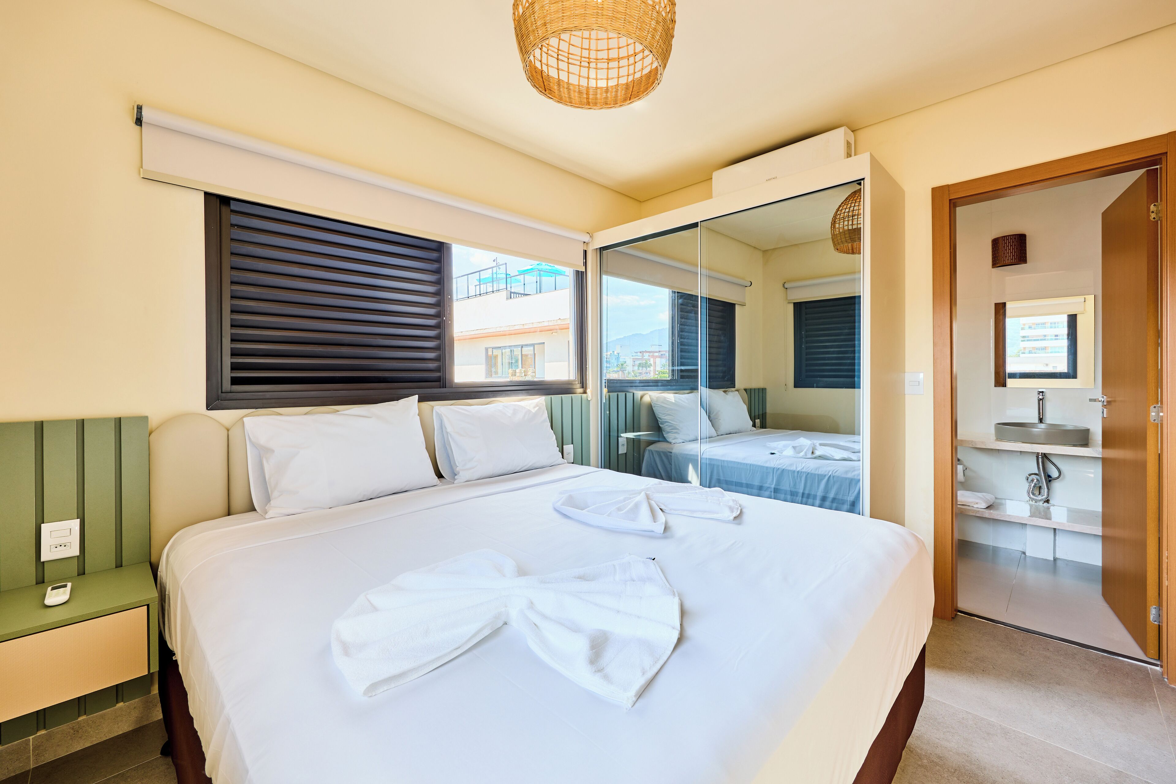 A hotel room with a large bed, a bedside table with a phone, a mirror, and a view of the outside.