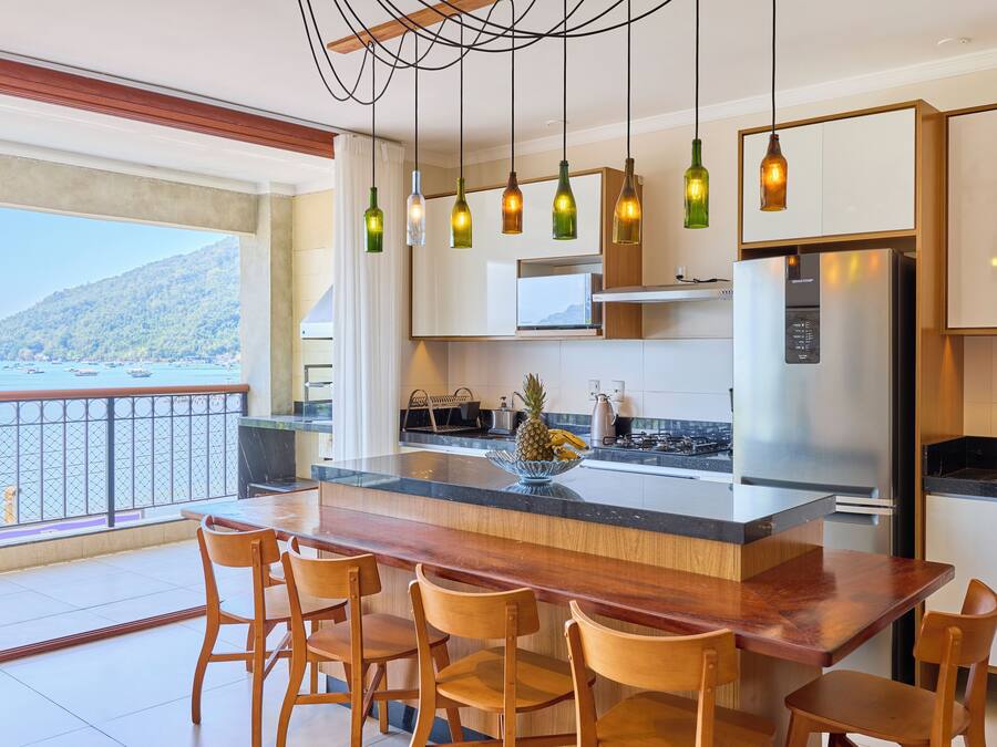 Una cocina moderna con una isla grande, sillas de madera y vista al mar.