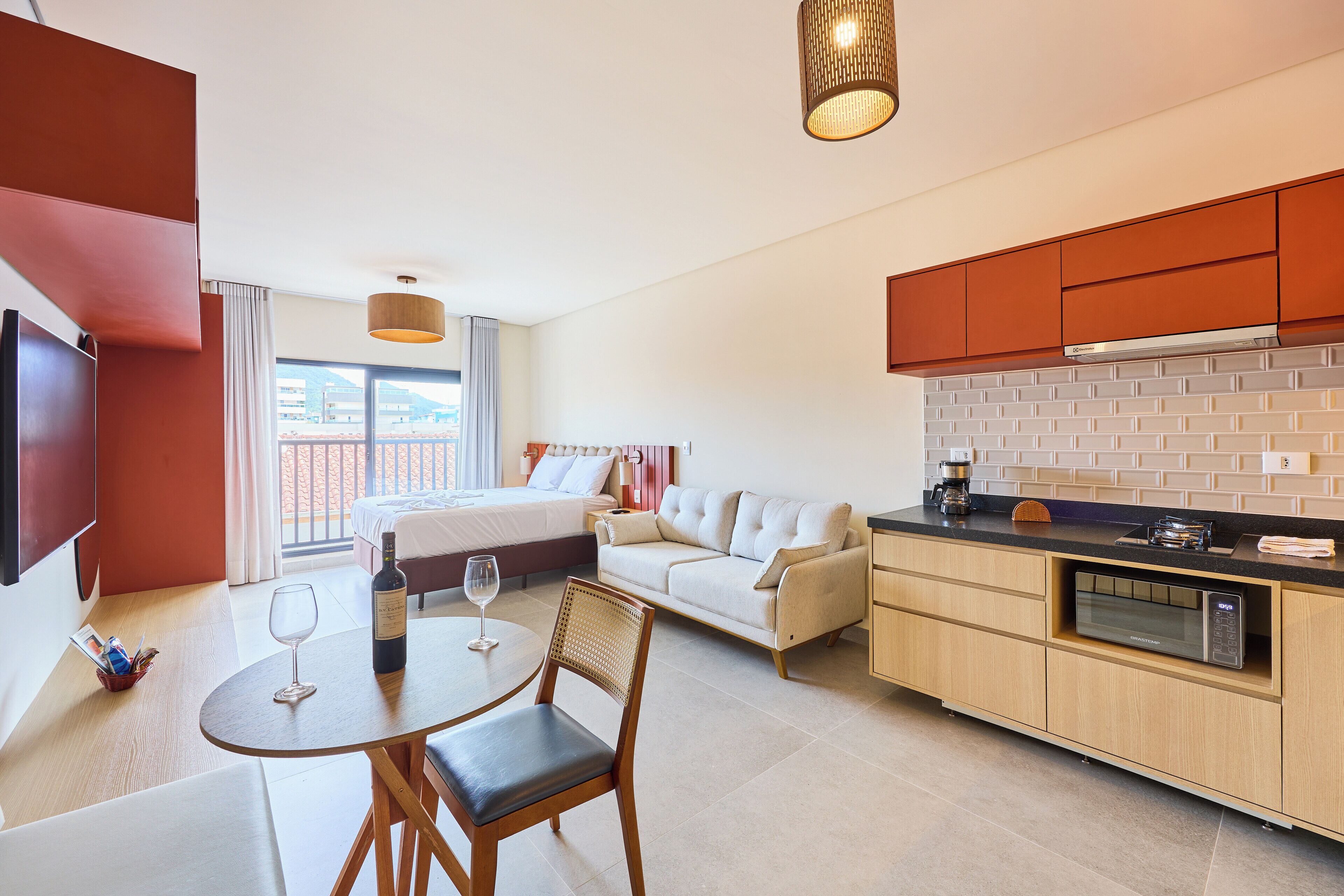 Una habitación de hotel moderna con una cama, un sofá, un comedor con mesa y sillas, una cocina con microondas y un ventanal con vistas.