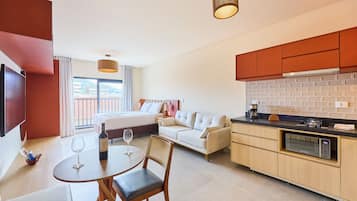 Una habitación de hotel moderna con una cama, un sofá, un comedor con mesa y sillas, una cocina con microondas y un ventanal con vistas.