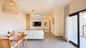 Un saló modern amb zona de menjador, un sofà, un televisor fixat a la paret i un finestra gran amb cortines.