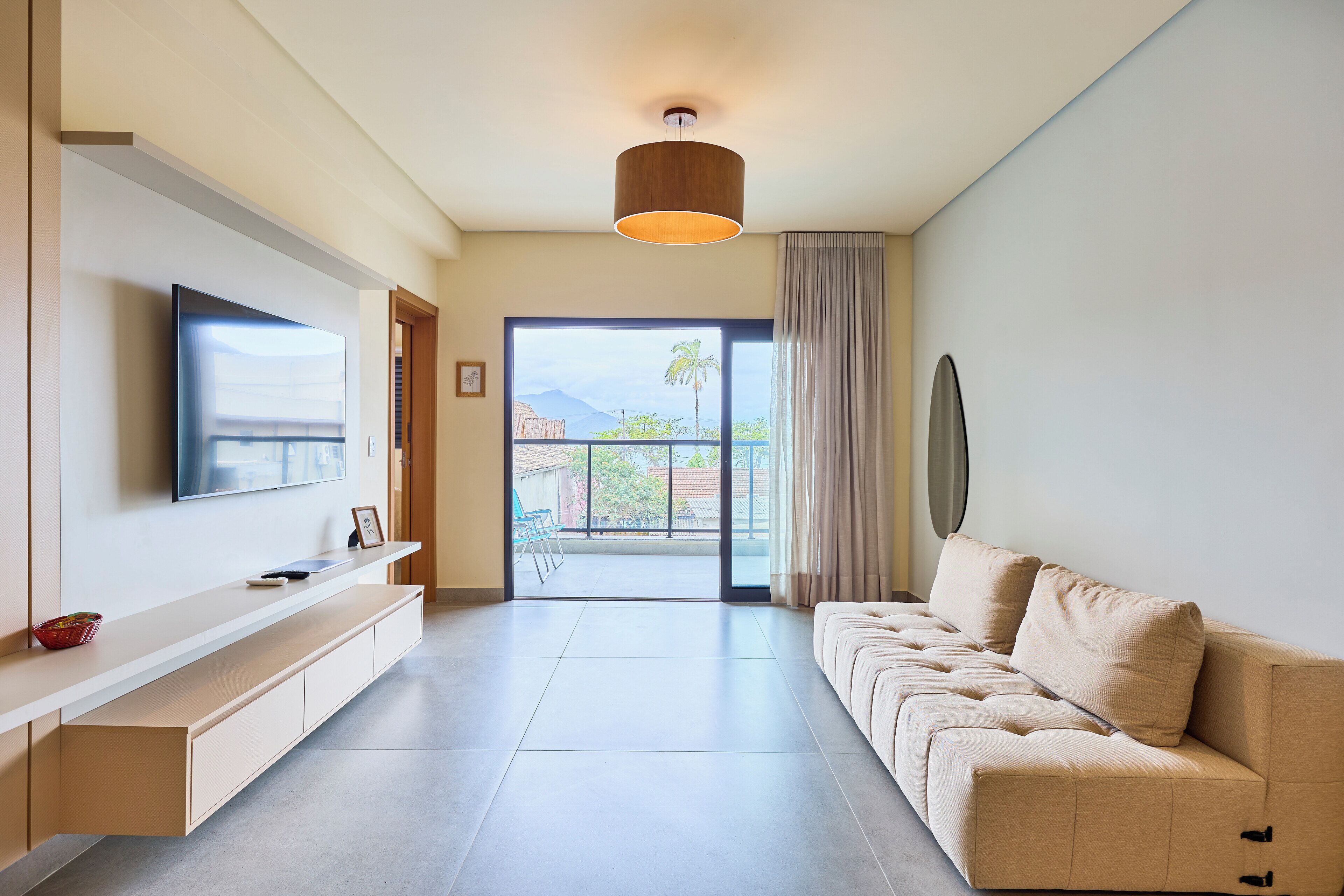 A modern living room with a flat-screen TV, a sofa, a built-in bench, and a view to the outside.