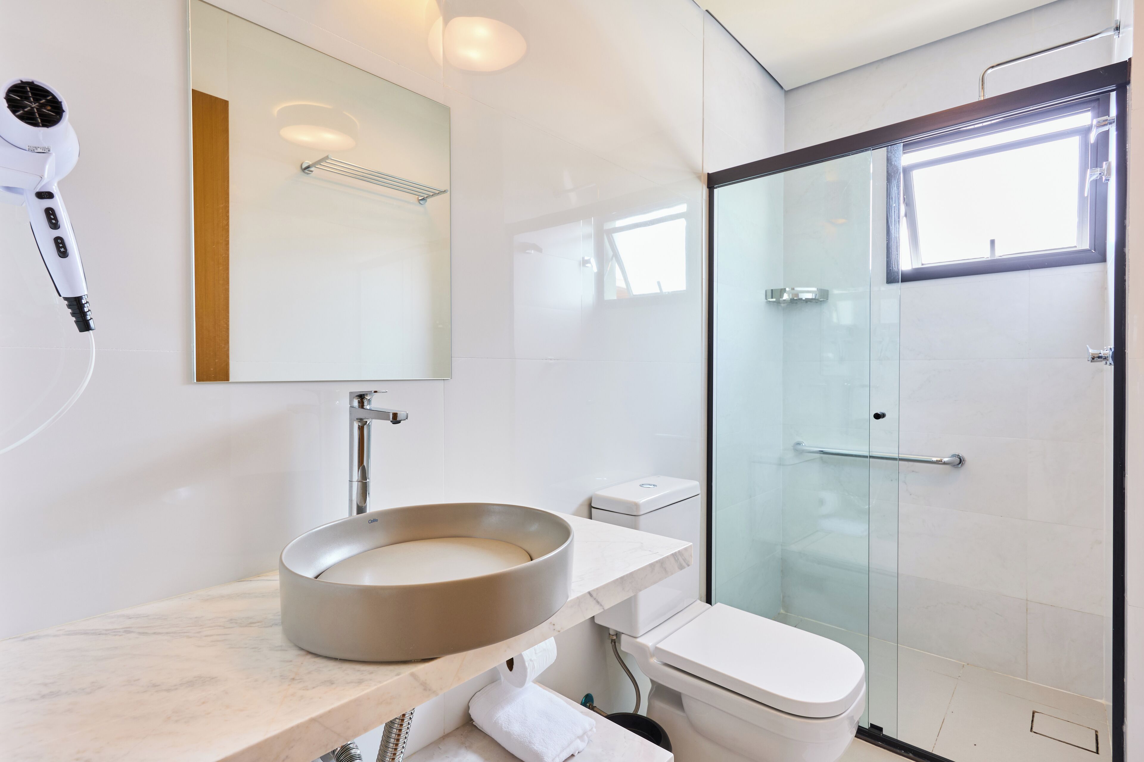 Ein modernes Badezimmer mit einem runden Waschbecken, einem Föhn, einer Duschkabine aus Glas und einer Toilette.