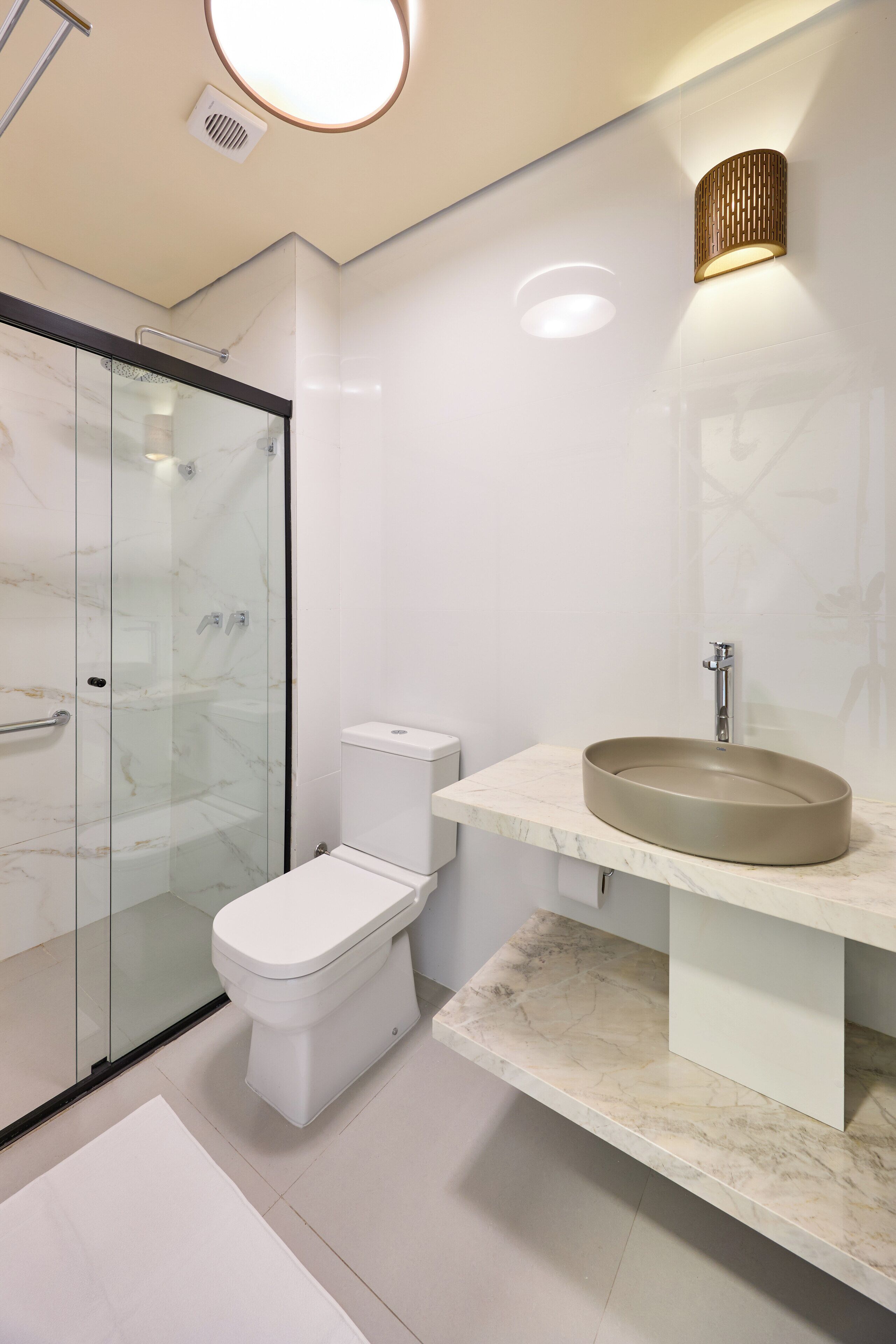 Ein modernes Badezimmer mit einer gläsernen Dusche, einer weißen Toilette und einem runden Waschbecken mit Marmorplatte.