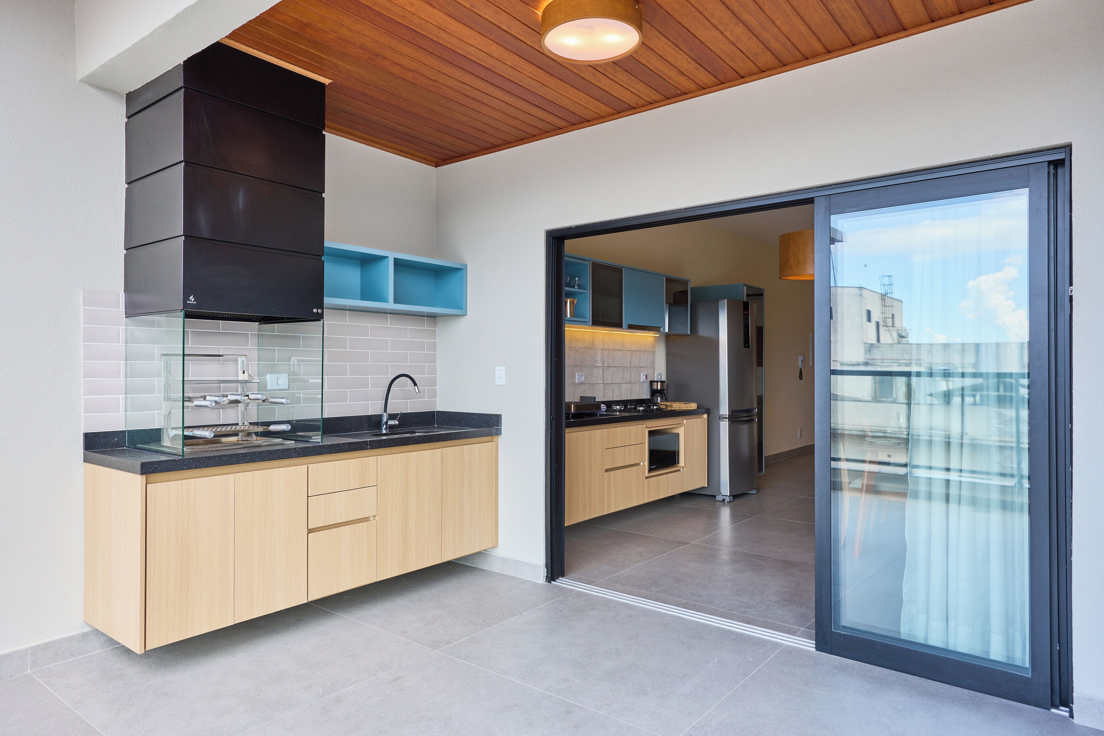 A modern kitchen with wooden cabinets, a black range hood, and a glass door leading to a balcony.