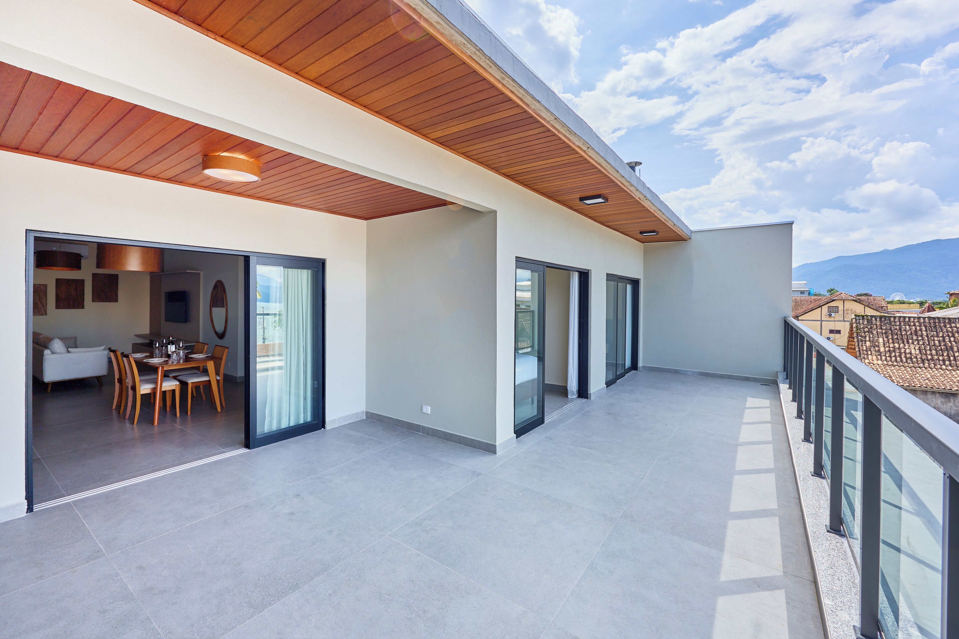 Een ruim balkon met houten plafond, glazen deuren naar een eethoek en uitzicht op het omliggende landschap.