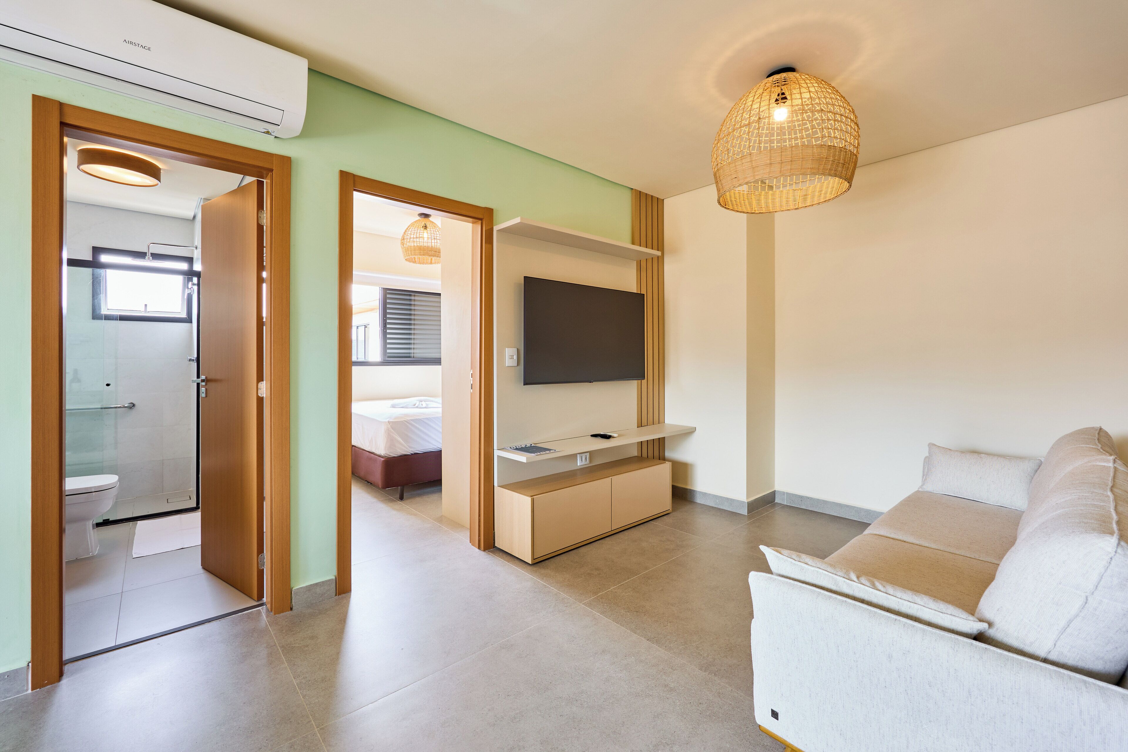 A modern living room with a sofa, a TV on a wooden stand, and a hanging light fixture.