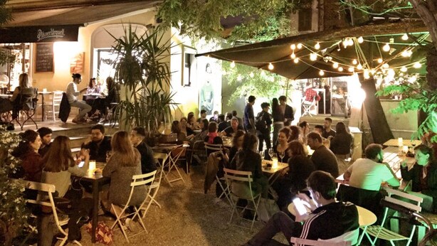 Un espace de restauration en plein air, avec des tables et des chaises, entouré de verdure et illuminé de guirlandes lumineuses.