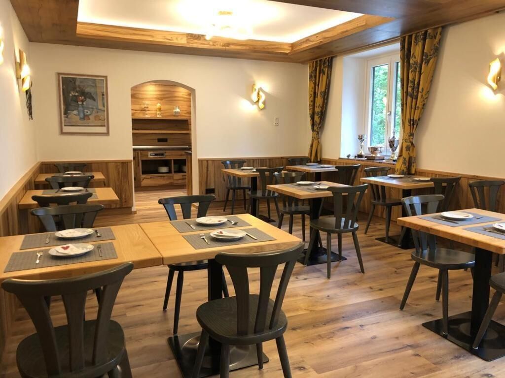 A restaurant with wooden tables and chairs, a wooden ceiling, and a window with curtains.
