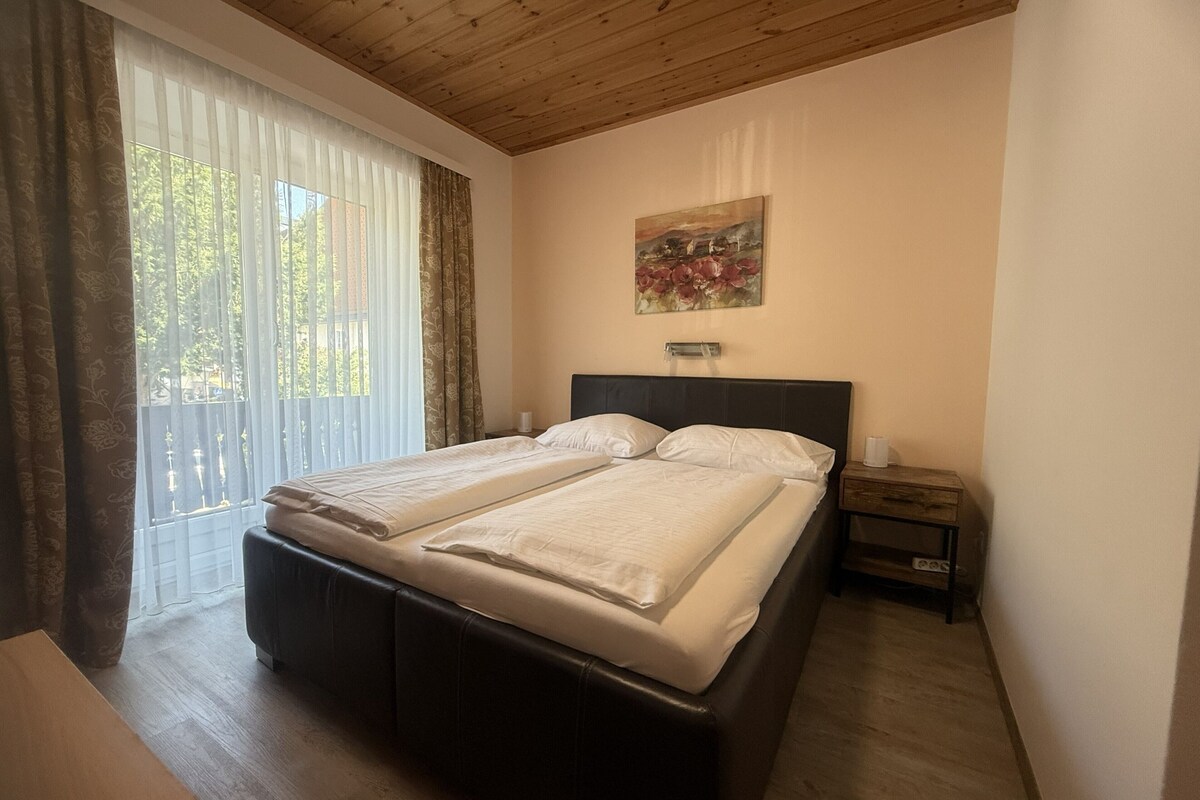 Una cama doble con cabecera, una mesita de noche con lámpara y una ventana con cortinas.