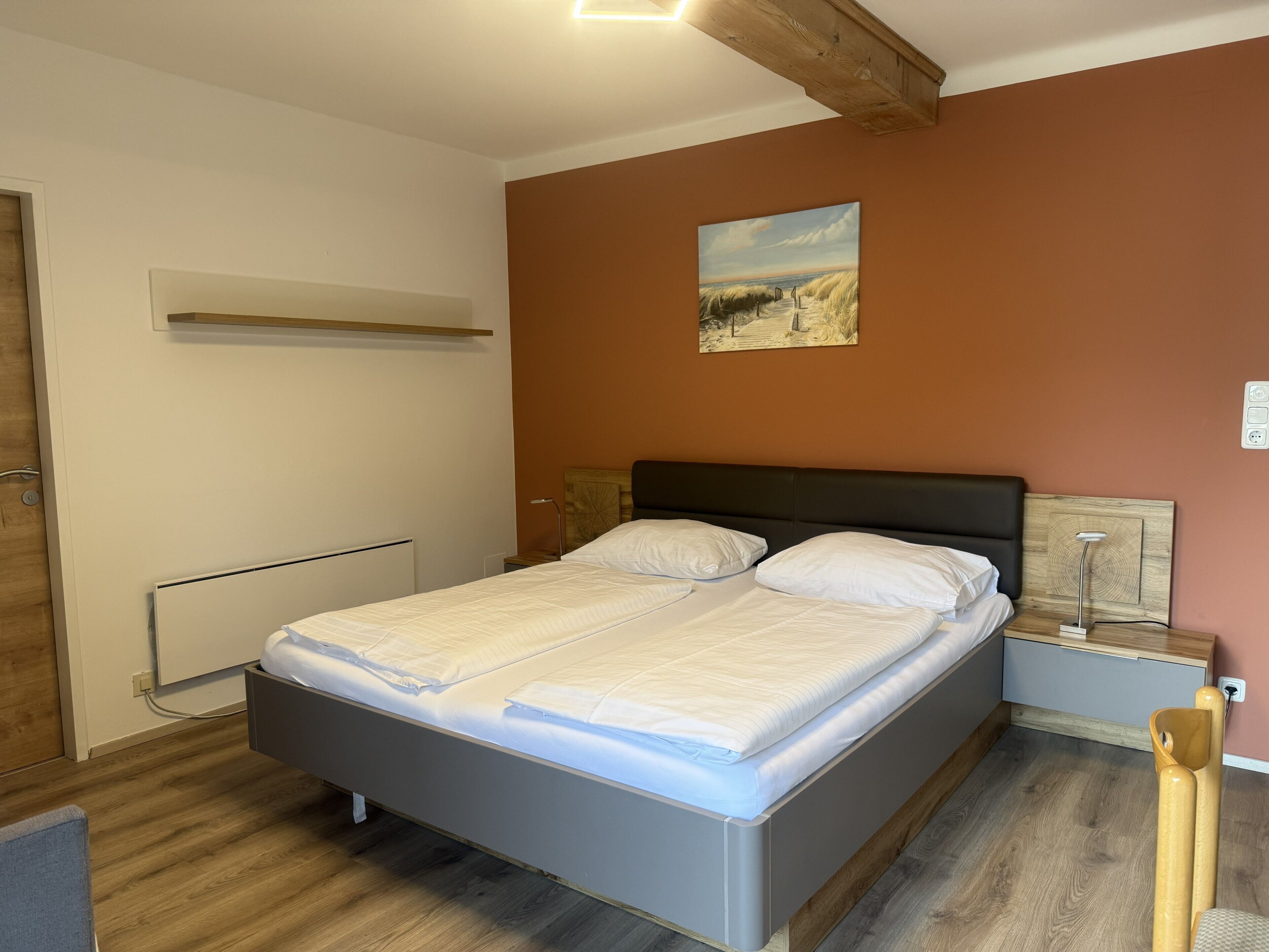 A bedroom with a bed, a nightstand, a wall-mounted shelf, and a painting.