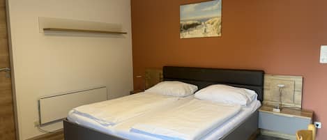 Un dormitorio con cama, mesita de noche, estante en la pared y un cuadro.