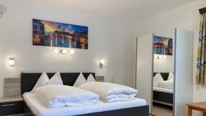 Un dormitorio moderno con cama, mesitas de noche, un espejo y una pintura de paisaje urbano en la pared.