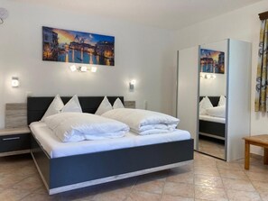 Un dormitorio moderno con cama, mesitas de noche, un espejo y una pintura de paisaje urbano en la pared.