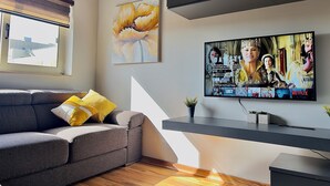 Ett modernt vardagsrum med en grå soffa, en stor platt-TV som är monterad på väggen och ett fönster med utsikt över en byggnad.