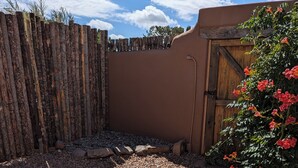 Un patio con una silla beige acolchada, cerca de madera, sendero de piedra y un arbusto con flores rojas.